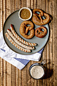 Bavarian traditional grilled pork sausages on ceramic plate served with german sweet mustard, mug of dark beer and pretzels
