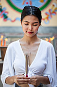 Young Asian woman in front of a Buddhist temple holding incense sticks (Bangkok, Thailand)