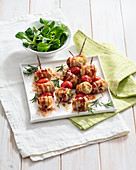 Filled bacon rolls with date tomatoes and rosemary on skewers
