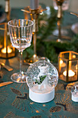 Weiße Maus in einer Schneekugel auf weihnachtlich gedecktem Tisch