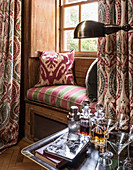 A 1930s Art Deco-style window seat and curtains with decanters and books in the foreground