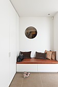 Brown scatter cushions on upholstered bench in hallway with fitted cupboards