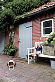 Junge auf einer Gartenbank neben Holzkisten vorm Backsteinhaus
