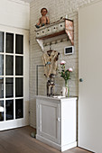 A doll on a vintage shelf above a white cabinet against a white-painted brick wall