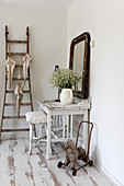 A white table with a shabby chic-style stool, a wall mirror and a ladder with old umbrellas