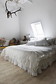 A double bed with white ruffles in a bedroom with deer antlers on the wall