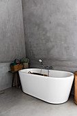 A freestanding bathtub in front of a grey wall