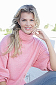 A young blonde woman wearing a pink turtle-neck jumper