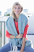 A young blonde woman wearing a coral-coloured jumper with a shawl over her shoulders