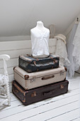 A stack of vintage suitcases and a dressmaker's dummy in an attic