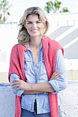 A young blonde woman wearing a denim shirt with a coral-coloured jumper over her shoulders