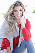 A young blonde woman wearing a red jumper with a light-coloured jumper over her shoulders