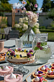 Kuchen, Törtchen und Dessertgläser auf gedecktem Tisch auf der Terrasse