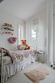 A bed with a floral cover in a white painted bedroom for a girl