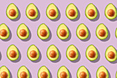Viele halbierte Avocados in Reihen auf lilafarbenem Untergrund