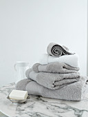 Stapel hellgraue Handtücher auf Marmortisch vor weißer Wand