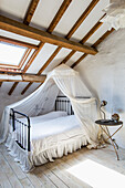 Bed with canopy and side table in rustic attic room with wood-beamed ceiling