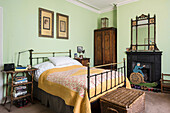 Original prints hang above French iron bed with Arts and Crafts ebonised and gilt mirror
