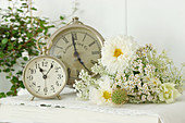 Vintage-style arrangement of cosmea, Queen Anne's lace, yarrow and snapdragons next to two clocks