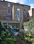 Ferns and yuccas in lush garden of brick house with extension