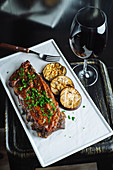 Grilled pork ribs garnished with fresh parsley served with sliced grilled eggplant on white tray