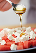 Honey being drizzled over watermelon and feta cheese