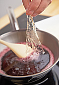 A soften sheet of gelatine being added to redcurrant juice