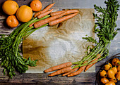 Various orange fruits arranged with bunches of fresh carrots on wooden tabl