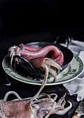 Uncooked meat of squids placed in metal bowl on table in kitchen on black background