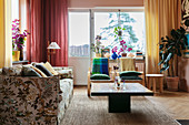An upholstered sofa with a floral pattern, a coffee table and colourful curtains in a living room