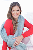 A young woman wearing a red jumper and white trousers with a shawl over her shoulders