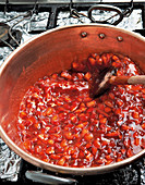 Konfitüre kochen - Erdbeeren in Stücke geschnitten im Topf rühren