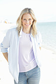 Blonde Frau in lila T-Shirt und blau-weiß gestreiftem Hemd am Meer