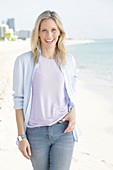 Blonde Frau in lila T-Shirt und blau-weiß gestreiftem Hemd am Meer