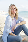 A blonde woman by the sea wearing a purple t-shirt and a blue-and-white striped shirt