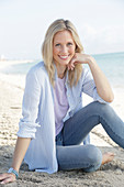 Blonde Frau in blau-weiß gestreiftem Hemd und Jeans am Meer