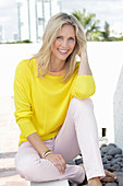 A blonde woman wearing a yellow jumper and white trousers