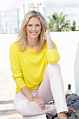 A blonde woman wearing a yellow jumper and white trousers