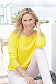 A blonde woman wearing a yellow jumper and white trousers