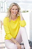 A blonde woman wearing a yellow jumper and white trousers