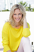 A blonde woman wearing a yellow jumper and white trousers