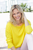 A blonde woman wearing a yellow jumper and white trousers