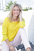 A blonde woman wearing a yellow jumper and white trousers