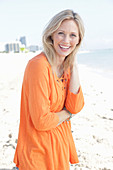 A blonde woman by the sea wearing an orange tunic