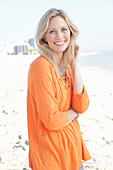 A blonde woman by the sea wearing an orange tunic