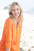 A blonde woman by the sea wearing an orange tunic