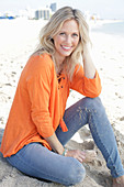 A blonde woman by the sea wearing an orange tunic and jeans