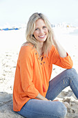 Blonde Frau in orangefarbener Tunikabluse und Jeans am Meer