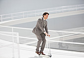 Businessman riding scooter down walkway
