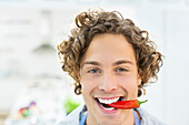 Smiling man holding chili pepper in mouth